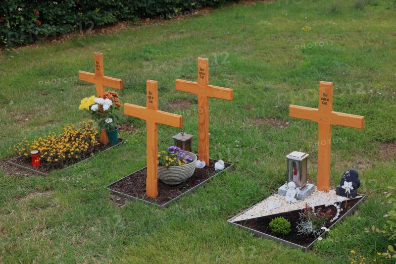 Flower decorated anonymous urn graves with wooden cross with inscription Here rests in God