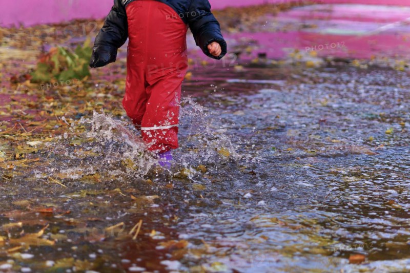 Child splashing water with boots and water pants in a puddle on a rainy day