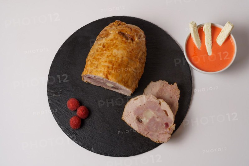 Close-up of a chicken stuffed with raspberry and goat cheese with a bowl of raspberry sauce isolated on white background
