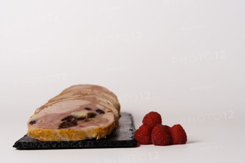 Close-up of a chicken stuffed with raspberry and goat cheese with a bowl of raspberry sauce isolated on white background