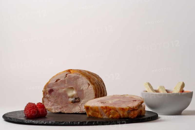 Close-up of a chicken stuffed with raspberry and goat cheese with a bowl of raspberry sauce isolated on white background