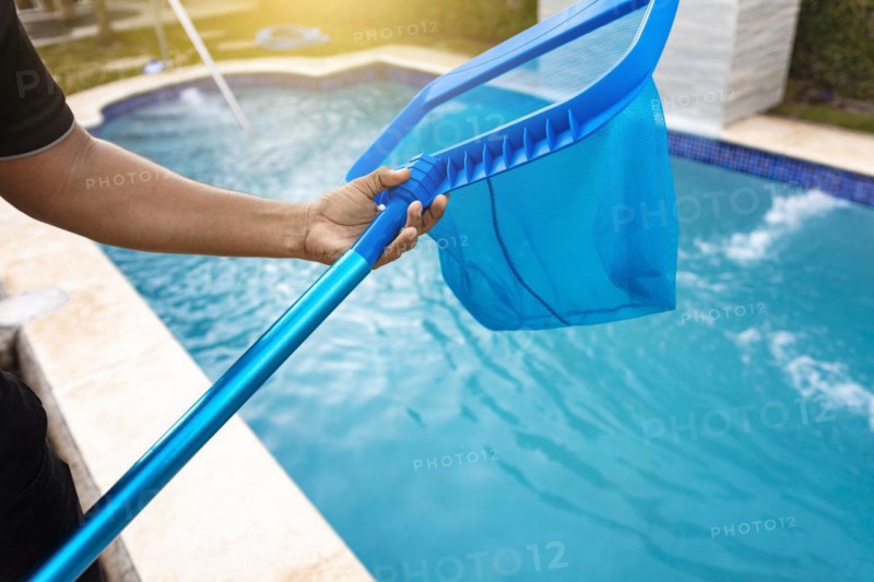 Person with skimmer cleaning pool