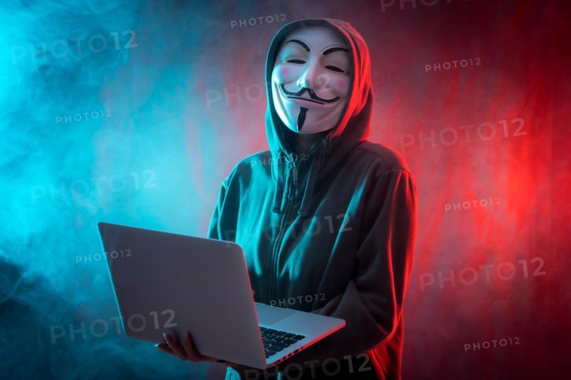 Hacker with anonymous mask with a computer and with a background of smoke and colored led