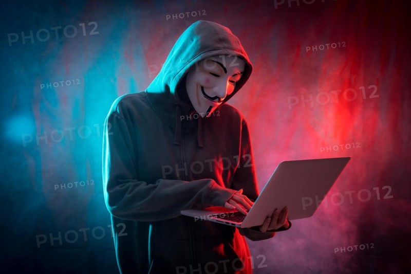Hacker with anonymous mask with a computer and with a background of smoke and colored led