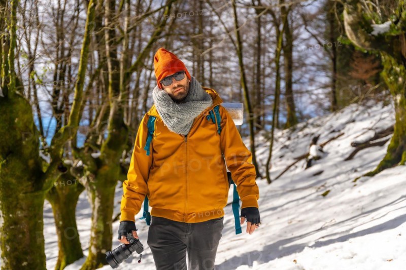 Portrait of a photographer trekking with a backpack taking photos in a beech forest with snow