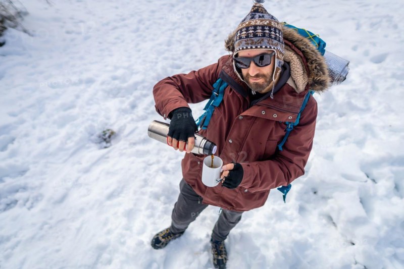 Portrait of man having breakfast a hot coffee from a thermos in winter in the snow before starting the trekking