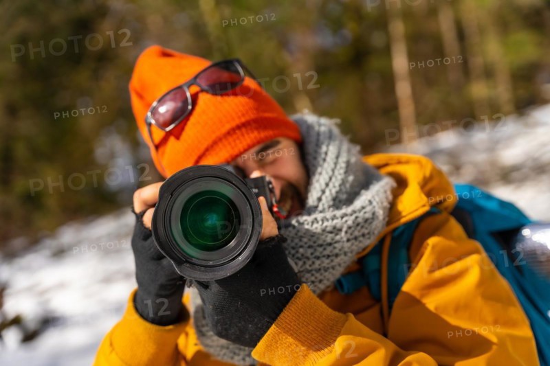 Portrait of a photographer taking winter photos in the mountains with snow doing a trekking with a backpack