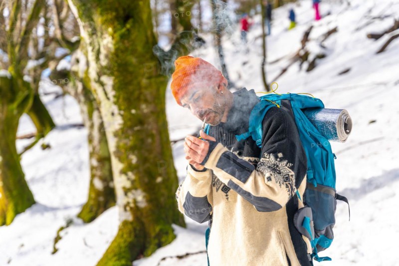 A man smoking lighting a cigarette with a lighter on a snowy mountain in winter