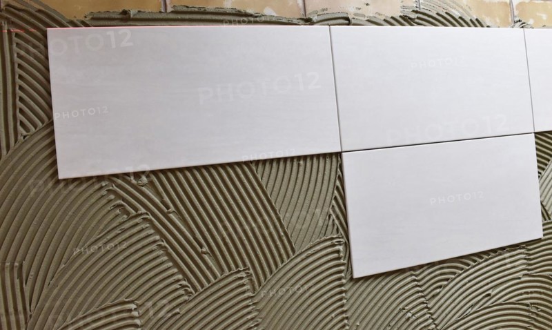 Tiler has applied tile adhesive and is sticking on new tiles