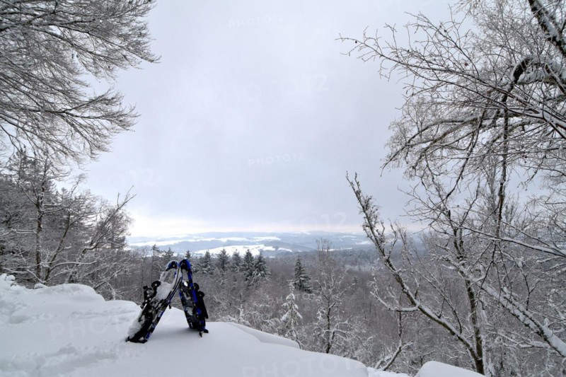 View from the mountain Moerschieder Burr in the Hunsrueck-Hochwald National Park of the snow-covered landscape with snowshoes in the foreground