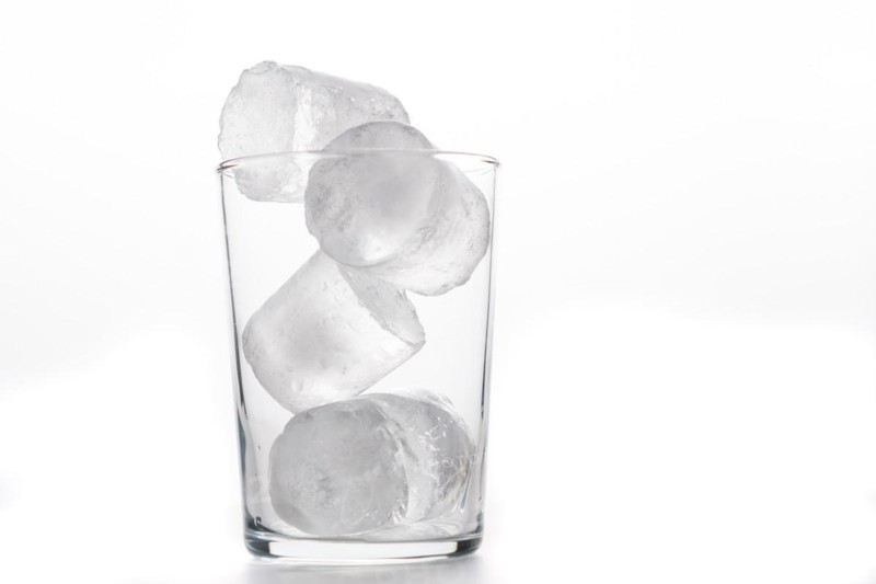Glass tumbler with ice cubes foreground white background and copy space