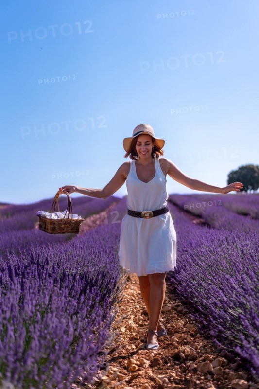 A caucasian woman in a summer lavender field with a hat picking flowers