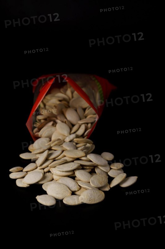 Roasted pumpkin seeds with salt coming out of their red bag on a black table with copy space