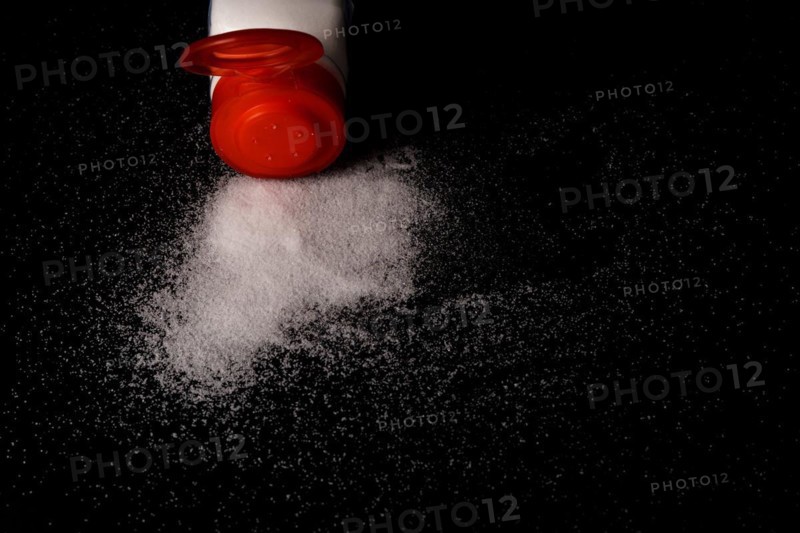 Close-up of a red salt shaker with spilled salt on a black table