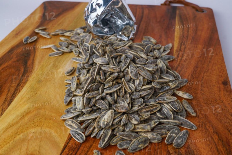 Roasted sunflower seeds with salt coming out of their bag on white background and copy space