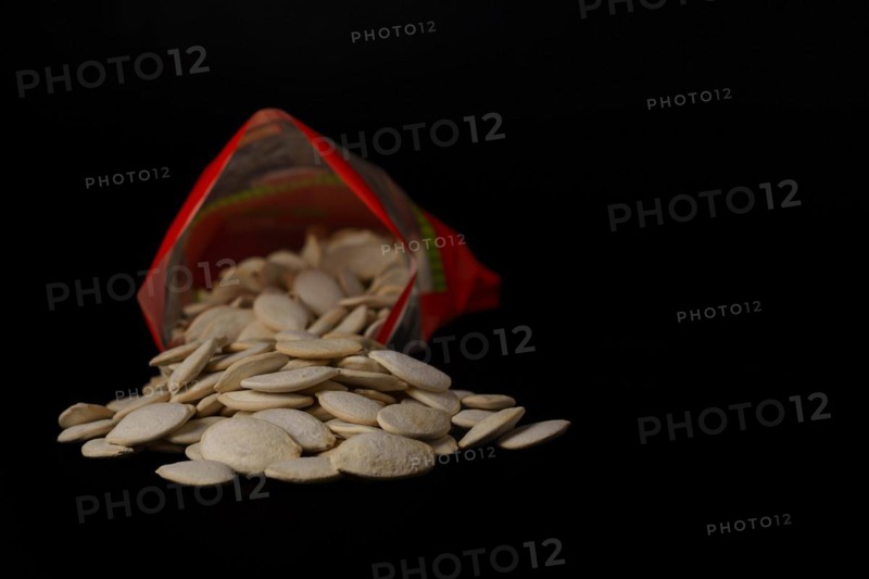 Roasted pumpkin seeds with salt coming out of their red bag on a black table with copy space