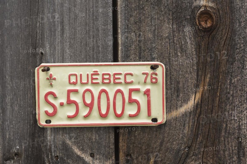 Vintage 1976 Quebec province license plate displayed on side wall of wood plank storage shed