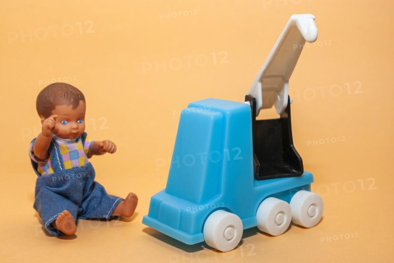 A car crane and a little dolls boy set against a beige background