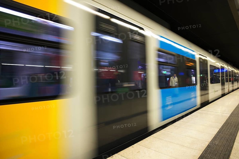 Travellers wearing Corona masks wait on the platform and are reflected in windows