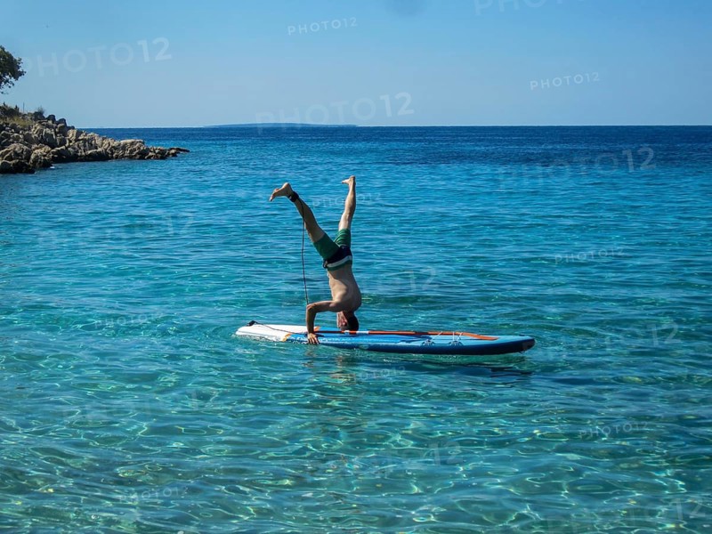 Man doing headstand on a SUP in crystal clear water