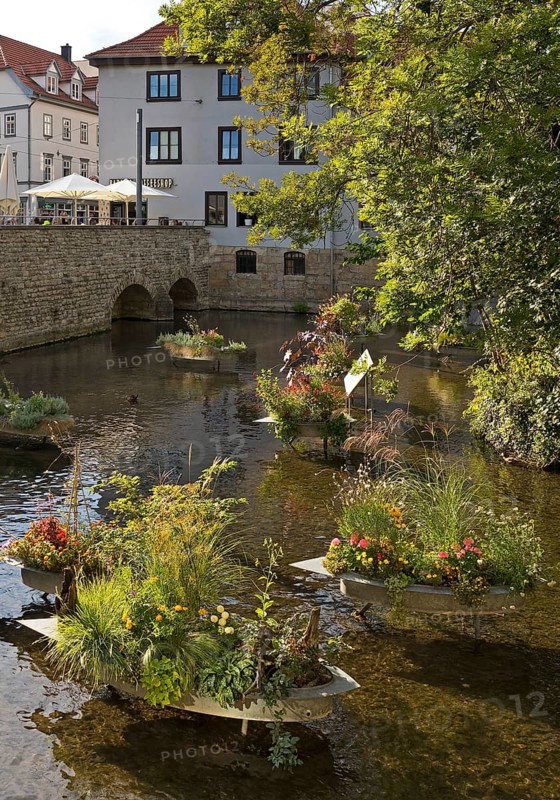 Zinc tubs in the shape of boats with flowering plants on the river Gera