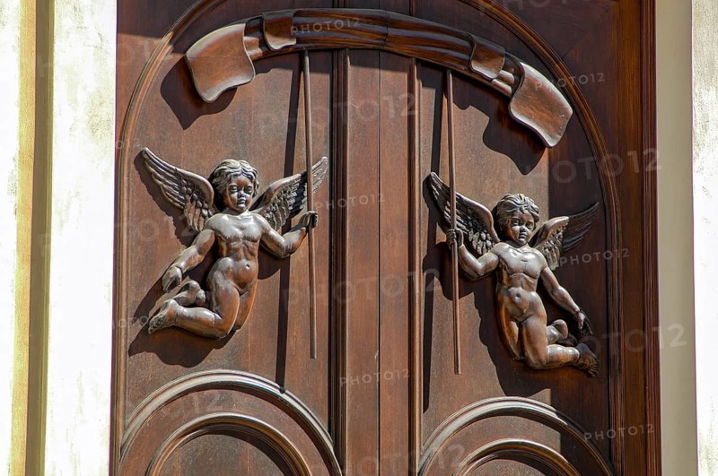Old wooden front door with attached wood carving in the shape of floating angels two angels with wings