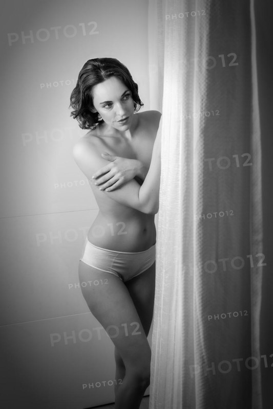Woman dressed only in panties stands behind a curtain