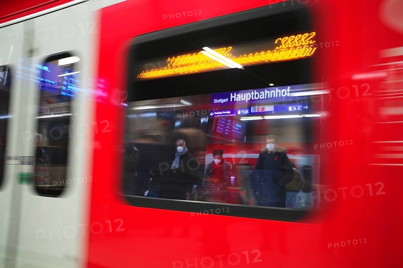 Travellers wearing Corona masks wait on the platform and are reflected in windows