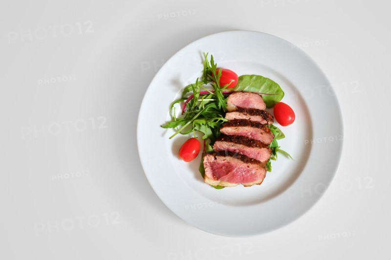 Top view of grilled duck breast medium rare served on a plate with arugula and corn salad