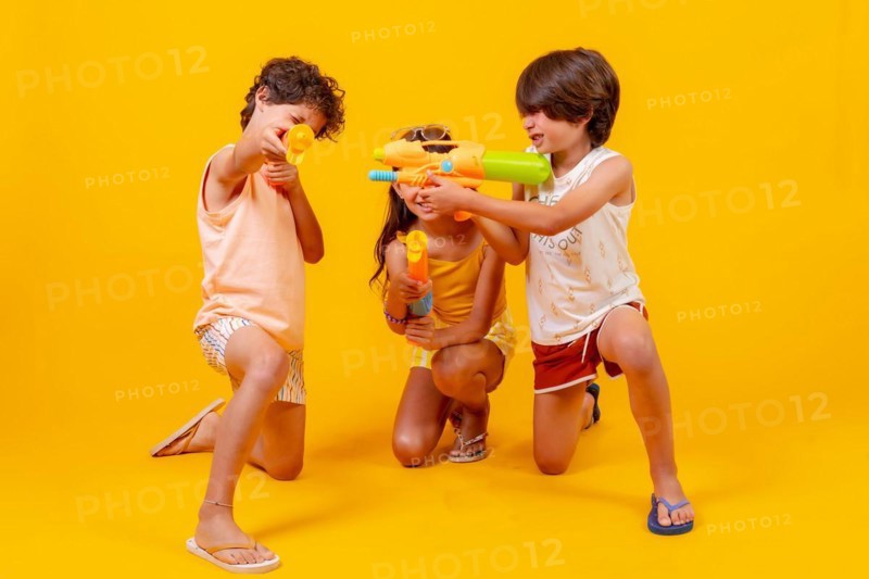 Kids having fun with water pistols on summer vacations and aiming at camera