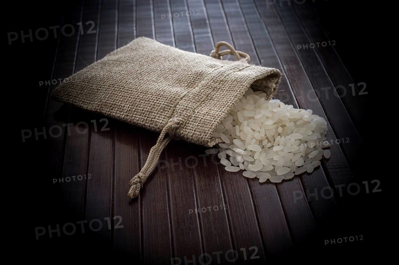 A straw pouch full of uncooked rice on a wooden background