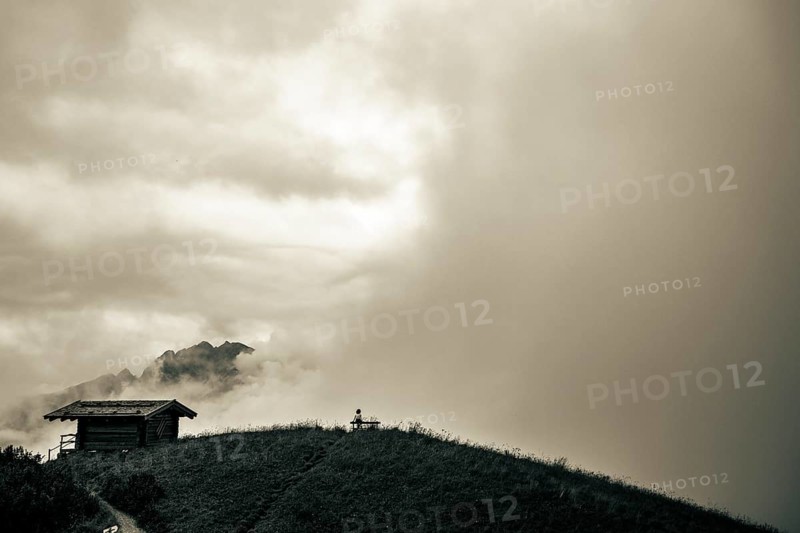 Mountain hut with bench and climber and dramatic clouds in the background