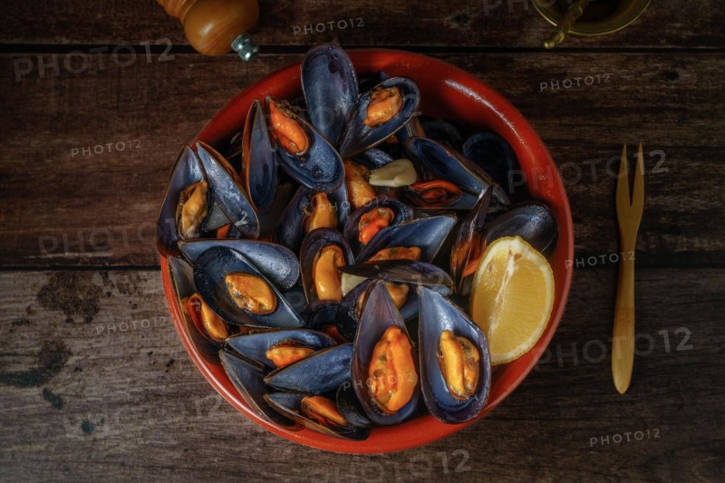 Steamed mussels with lemon in clay pot with metal mortar and pepper shaker