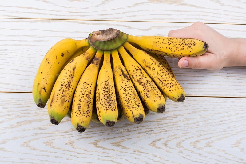 Hand holding bunch of freckled bananas on a wooden texture