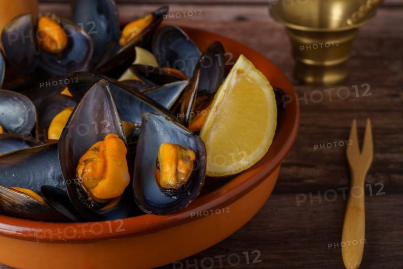 Steamed mussels with lemon in clay pot with metal mortar and pepper shaker