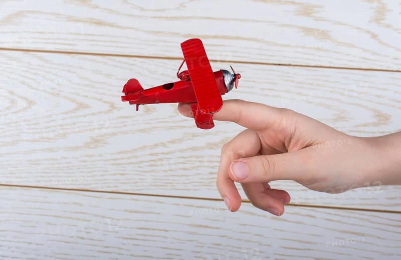 Hand holding a red toy plane on a on wooden texture