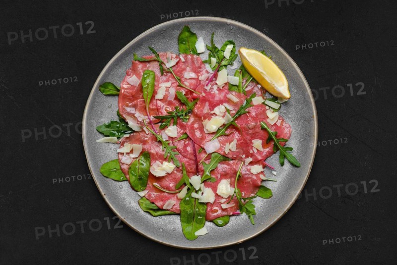 Top view of marbled beef carpaccio with arugula and chard leaves