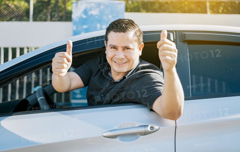 Happy driver giving a thumbs up on the road. safe driving concept. Satisfied driver man showing thumb up. Young driver man in the car showing thumb up