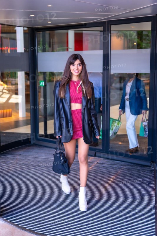 Portrait of a Caucasian girl in a red dress walking out of the revolving door of the shopping center