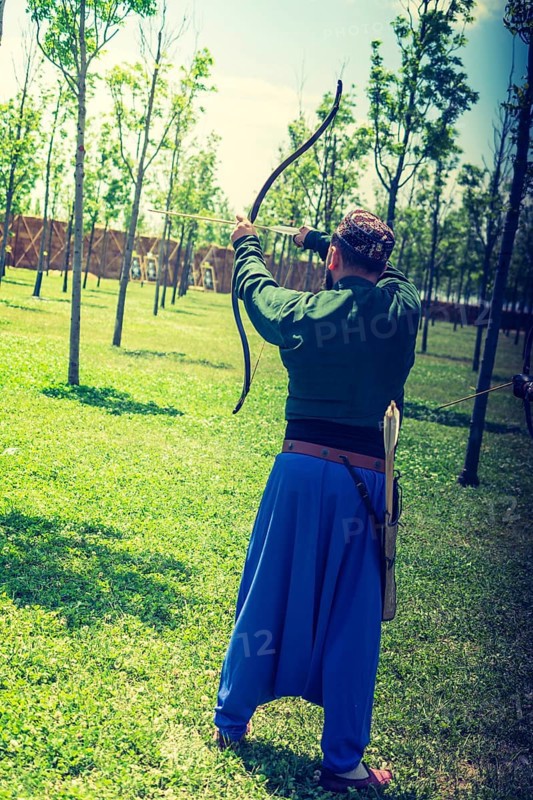 Archer with bow in traditional clothes shooting an arrow