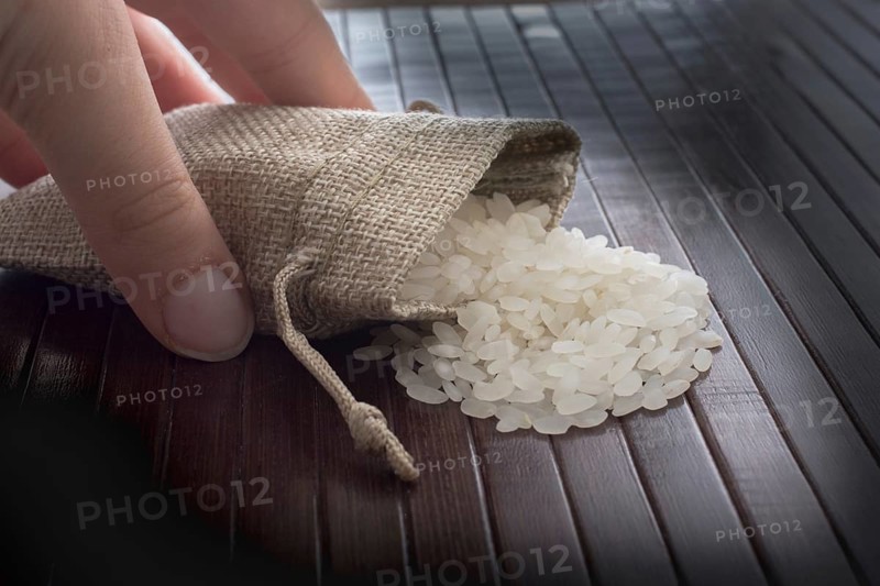 Hand holding straw pouch full of uncooked rice on a wooden background