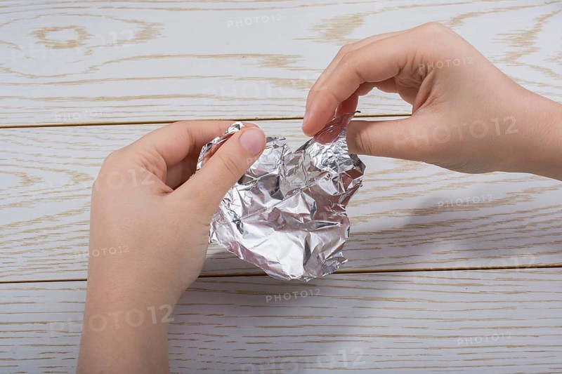 Hand tearing a heart shaped aluminium foil on a wooden background