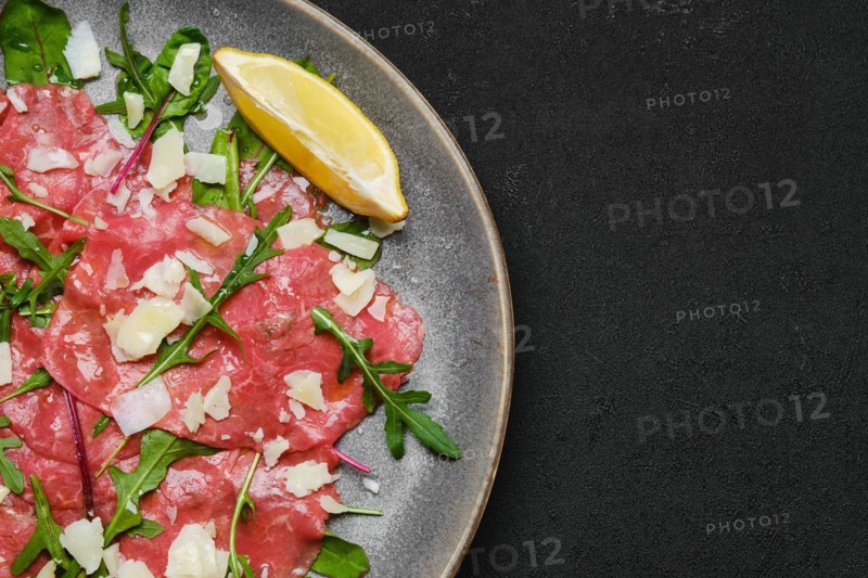 Top view of marbled beef carpaccio with arugula and chard leaves