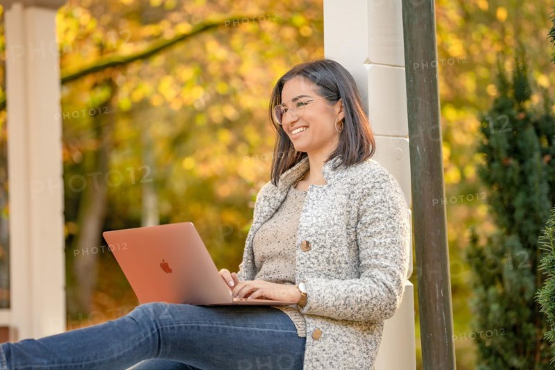 Pretty woman with glasses and MacBook in hand sits in the park at autumn time