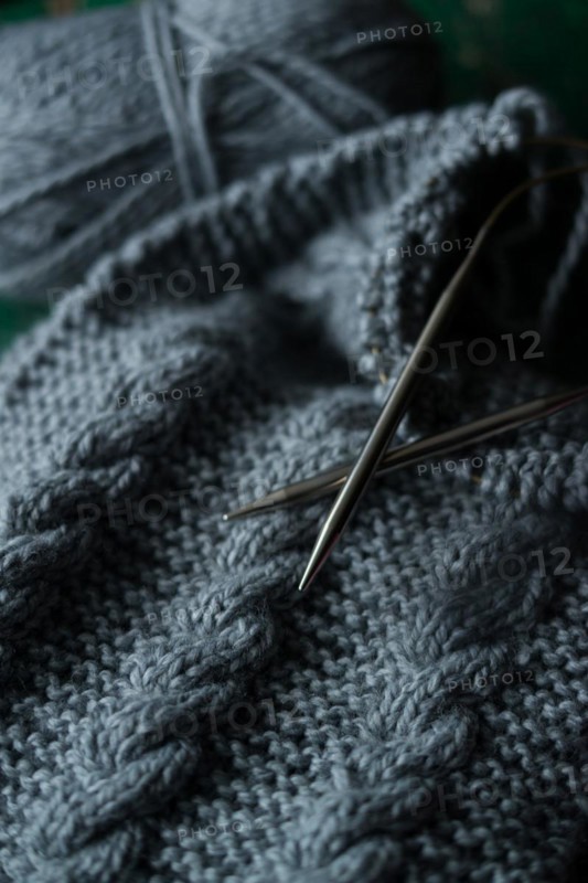 Grey knitted piece with knitting pattern and knitting needles