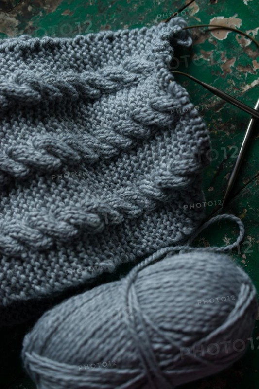 Grey knitted piece with knitting pattern and knitting needles