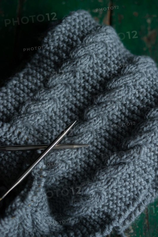 Grey knitted piece with knitting pattern and knitting needles