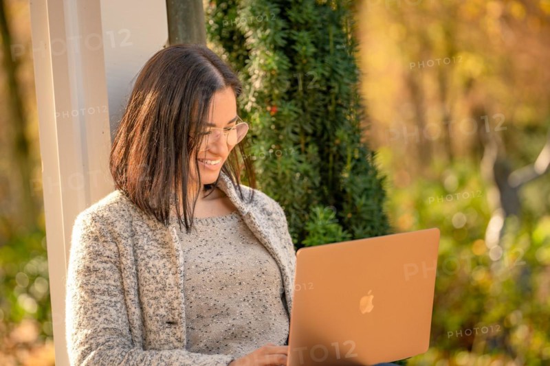 Pretty woman with glasses and MacBook in hand sits in the park at autumn time