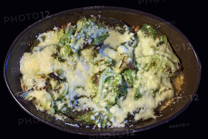 Kale gratinated with cheese and minced meat in an earthenware casserole on a black background