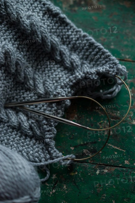 Grey knitted piece with knitting pattern and knitting needles